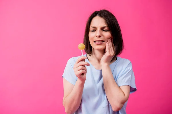 Junge Frau mit empfindlichen Zähnen isst süßen Lutscher auf farbigem Hintergrund — Stockfoto