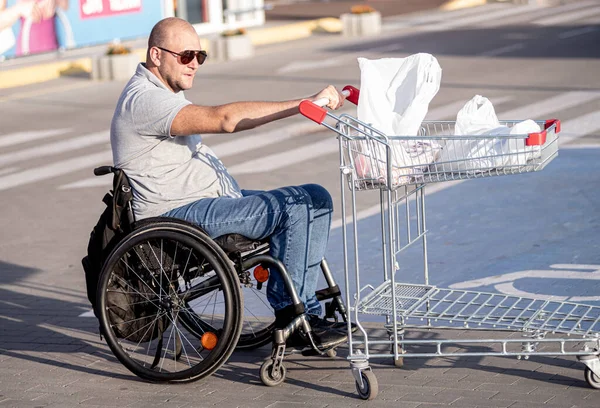 Persona con una discapacidad física empujando carro delante de sí mismo en el estacionamiento del supermercado —  Fotos de Stock