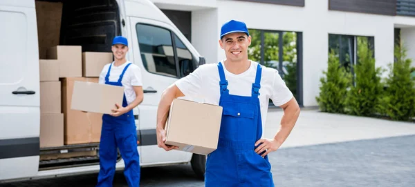 Dos trabajadores de la empresa de mudanzas descargan cajas de minibús en un nuevo hogar — Foto de Stock