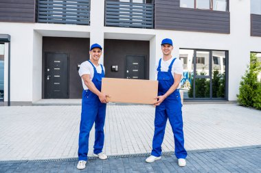 İki nakliye şirketi çalışanı minibüsten yeni eve kutular boşaltıyor.