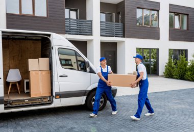 Two removal company workers are loading boxes into a minibus. clipart