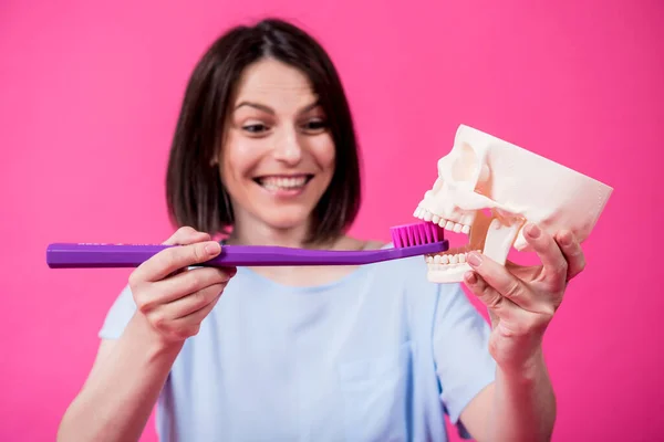Schöne Frau beim Zähneputzen eines künstlichen Schädels mit einer großen Zahnbürste — Stockfoto