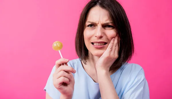 Wanita muda dengan gigi sensitif makan permen manis di latar belakang warna — Stok Foto