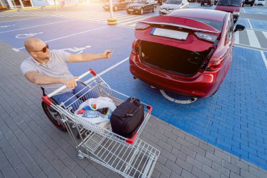 Fiziksel engelli biri alışverişi süpermarketin otoparkında bir arabanın bagajına koyar.