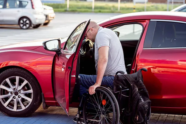 Person med fysisk funktionsnedsättning att komma i röd bil från rullstol — Stockfoto