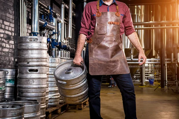 Deri önlüklü genç bira imalathanesinde bira fıçısı tutuyor. — Stok fotoğraf