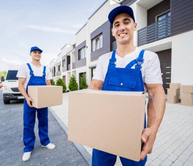 İki nakliye şirketi çalışanı minibüsten müşterilerin evlerine kutu indiriyor.