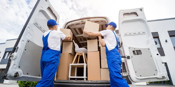 Dois trabalhadores da empresa de remoção estão carregando caixas e móveis em um microônibus. — Fotografia de Stock