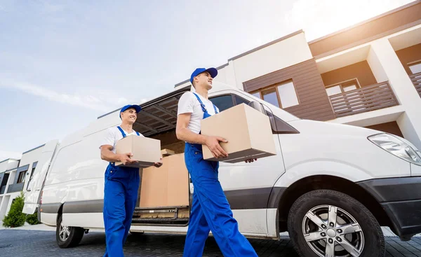 İki nakliye şirketi çalışanı minibüsten müşterilerin evlerine kutu indiriyor.