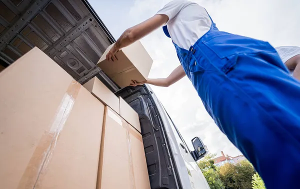 Két költöztető cég dolgozója dobozokat pakol ki a kisbuszból. — Stock Fotó