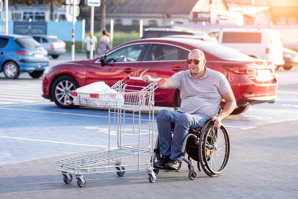 Fiziksel engelli bir insan süpermarketin önünde el arabasını itiyor. — Stok fotoğraf
