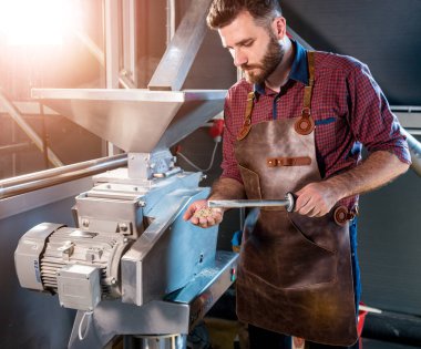 Deri önlüklü genç bir bira üreticisi modern bir bira fabrikasında malt tohumlarının öğütülmesini kontrol eder.