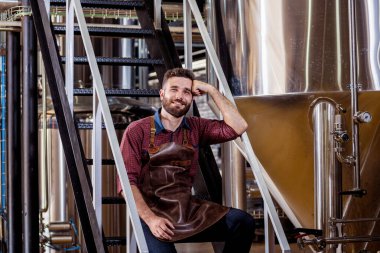 Modern bira fabrikasında deri önlüklü genç bir bira imalatçısı.