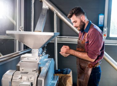 Deri önlüklü genç bir bira üreticisi modern bir bira fabrikasında malt tohumlarının öğütülmesini kontrol eder.