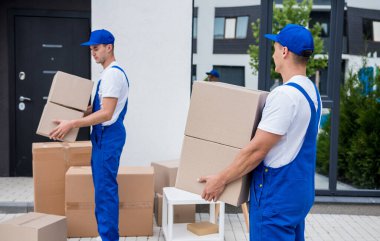 İki nakliye şirketi çalışanı bir minibüse kutu yüklüyorlar..