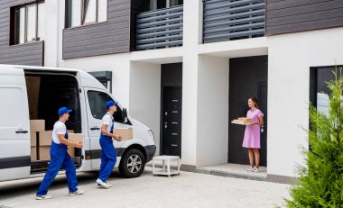 İki nakliye şirketi çalışanı minibüsten müşterilerin evlerine kutu indiriyor.