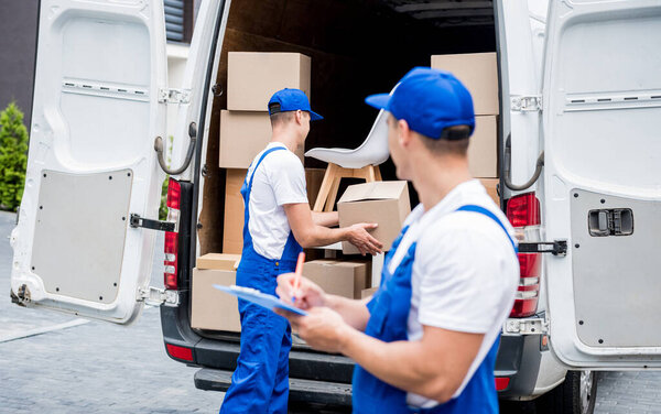 Two removal company workers unloading boxes from minibus into customers home