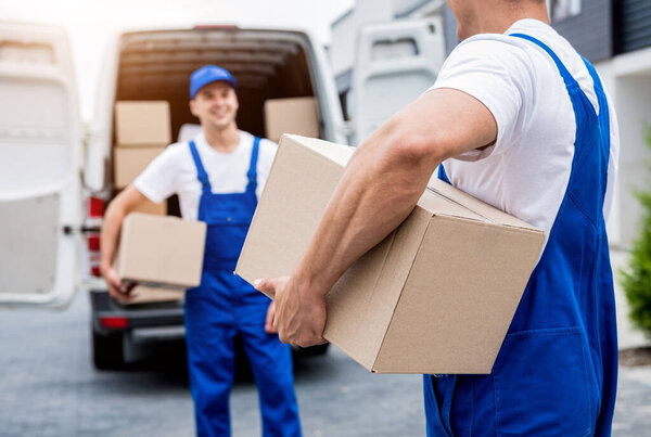 Two removal company workers unloading boxes from minibus into customers home