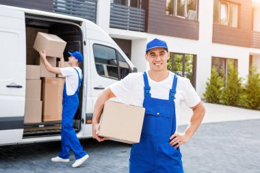 İki nakliye şirketi çalışanı minibüsten yeni eve kutular boşaltıyor.