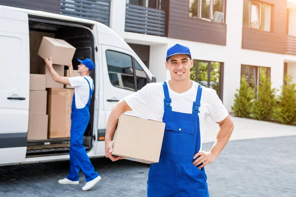 İki nakliye şirketi çalışanı minibüsten yeni eve kutular boşaltıyor.