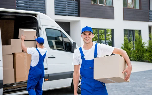 İki nakliye şirketi çalışanı minibüsten yeni eve kutular boşaltıyor.