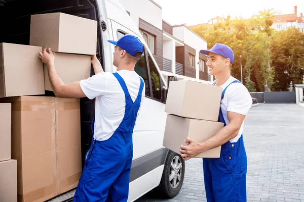 İki nakliye şirketi çalışanı minibüsten yeni eve kutular boşaltıyor.