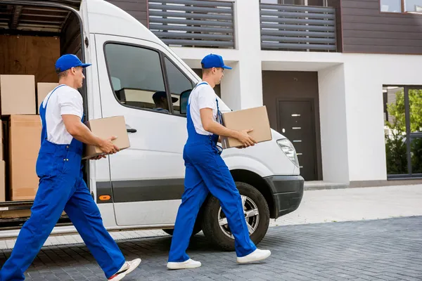 Two removal company workers unloading boxes from minibus into new home — Stock Photo, Image