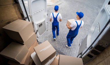 İki nakliye şirketi çalışanı minibüsten kutuları boşaltıyor.