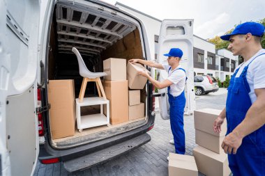 İki nakliye şirketi çalışanı bir minibüse kutu ve mobilya yüklüyorlar..