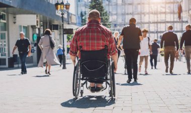Tekerlekli sandalyede fiziksel engelli genç bir adam sokakta yürüyor.