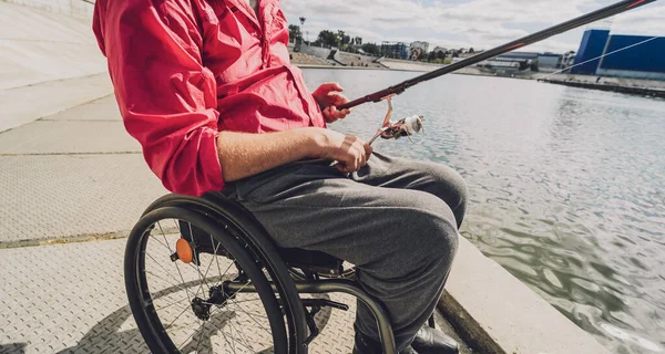 Persona con discapacidad física en una silla de ruedas que pesca desde el muelle de pesca. — Foto de Stock
