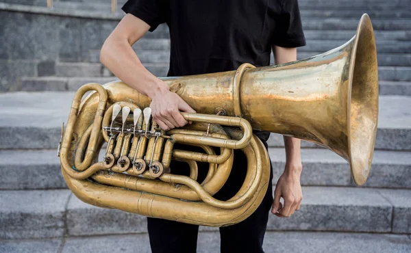 Giovane musicista di strada che suona la tuba seduto su gradini di granito — Foto Stock