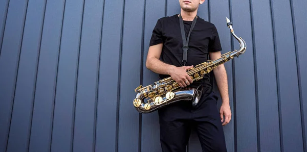 Jovem músico de rua tocando saxofone perto da grande parede azul — Fotografia de Stock