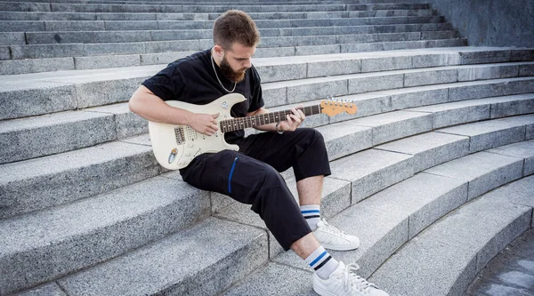 年轻的街头音乐家坐在花岗岩台阶上弹奏吉他 — 图库照片