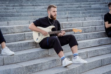 Gitar çalan genç sokak müzisyeni granit merdivenlerde oturuyor.