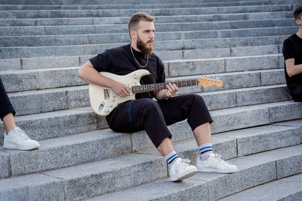 Young street musician playing guitar sitting on granite steps — Stock Photo, Image
