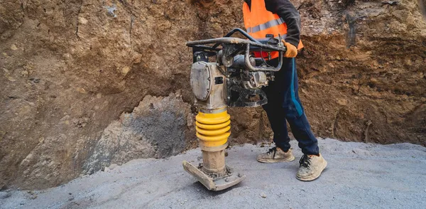 Lavoratore utilizza un costipatore di vibrazioni portatile nella costruzione di una sottostazione di trasmissione di energia — Foto Stock