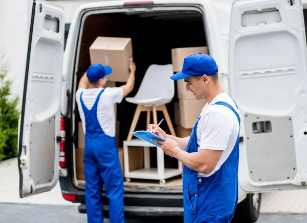 Dos trabajadores de la empresa de mudanzas descargan cajas de minibús en un nuevo hogar — Foto de Stock