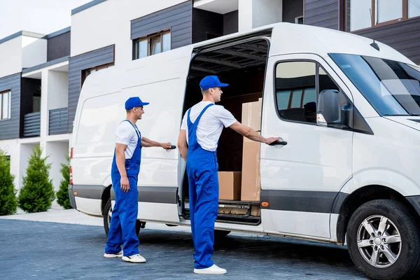 Dos trabajadores de la empresa de mudanzas están cargando cajas en un minibús. —  Fotos de Stock