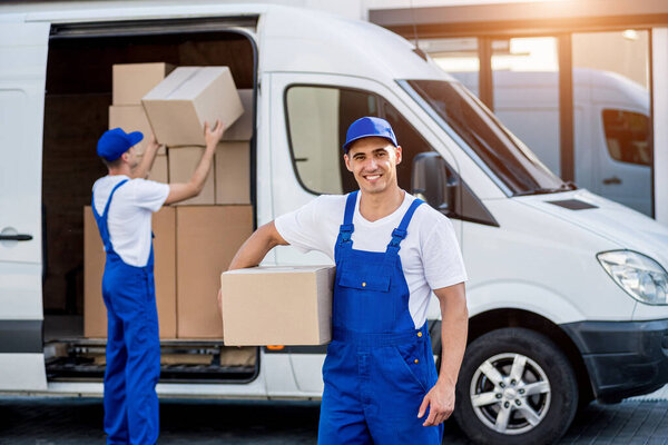 Two removal company workers unloading boxes from minibus into new home