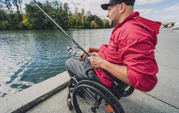 Persona con discapacidad física en una silla de ruedas que pesca desde el muelle de pesca. — Foto de Stock