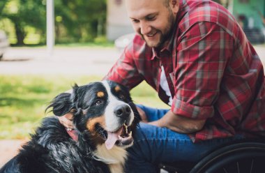Köpeğiyle birlikte tekerlekli sandalyede fiziksel engelli mutlu bir genç adam..