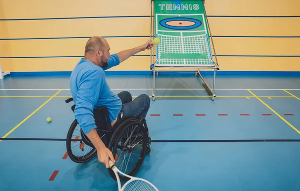 Дорослий чоловік з фізичною вадою в інвалідному візку грає в теніс на критому тенісному корті — стокове фото