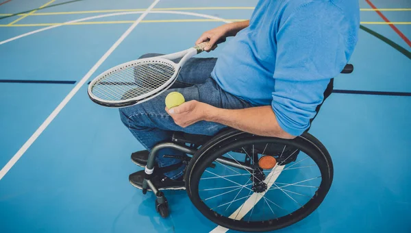 Взрослый мужчина с ограниченными физическими возможностями в инвалидной коляске играет в теннис на крытом теннисном корте — стоковое фото