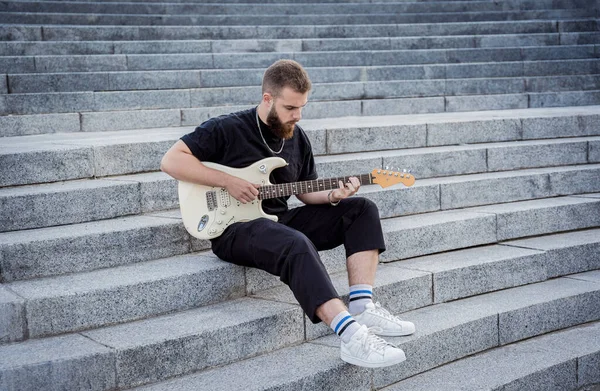 Jovem músico de rua tocando guitarra sentado em degraus de granito — Fotografia de Stock