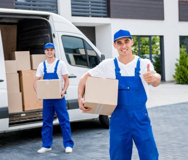 İki nakliye şirketi çalışanı minibüsten yeni eve kutular boşaltıyor.