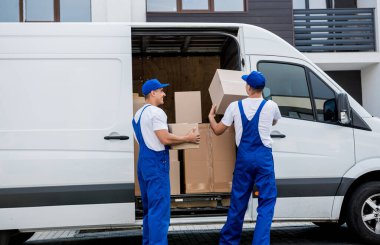 İki nakliye şirketi çalışanı minibüsten yeni eve kutular boşaltıyor.