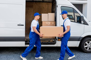 İki nakliye şirketi çalışanı minibüsten yeni eve kutular boşaltıyor.