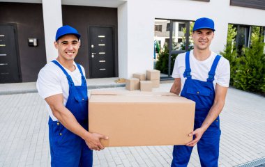 İki nakliye şirketi çalışanı minibüsten yeni eve kutular boşaltıyor.