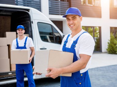 İki nakliye şirketi çalışanı minibüsten yeni eve kutular boşaltıyor.